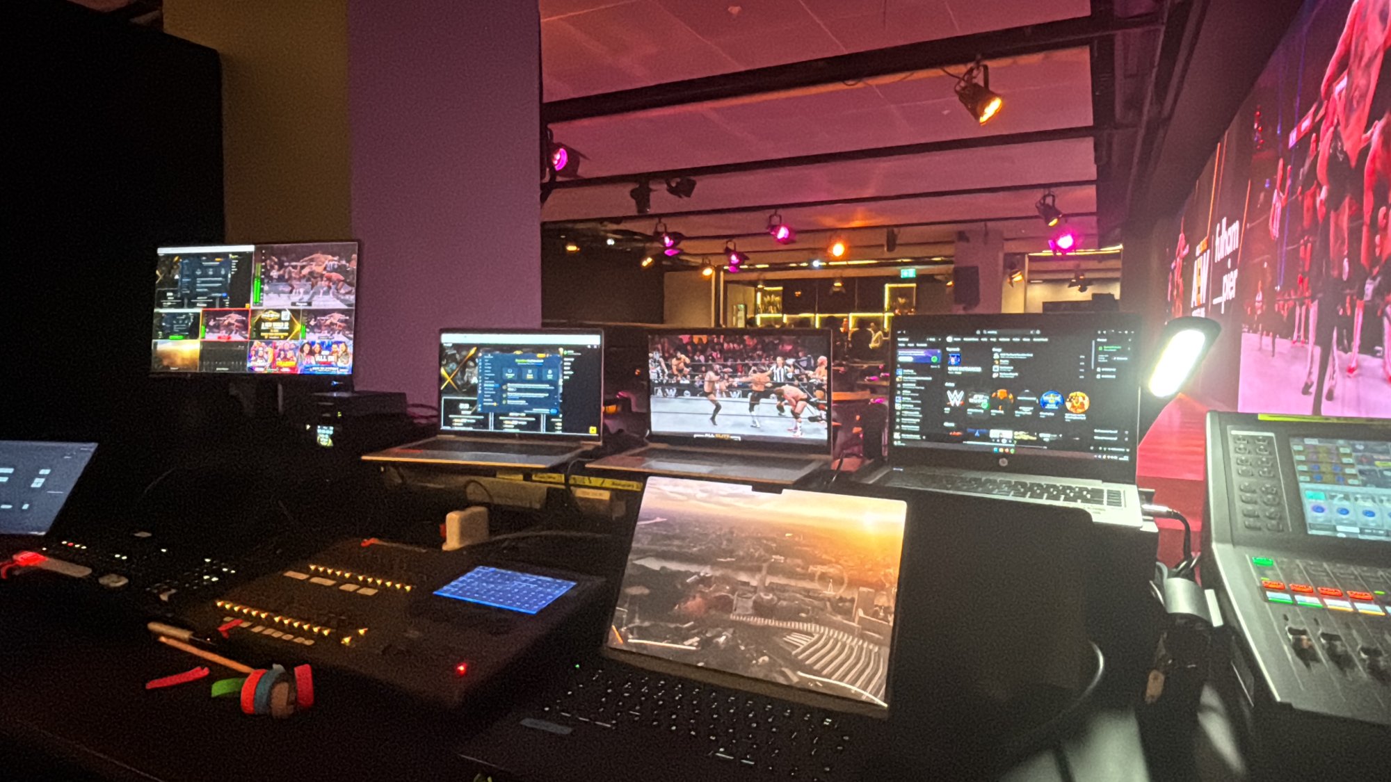 Operator position with several laptops, a monitor and audio and lighting controllers facing a screen wall