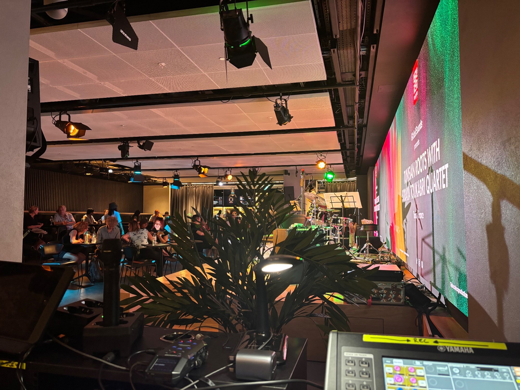 Venue with a large LED screen wall, stage lighting and a live band, seen from the technical position
